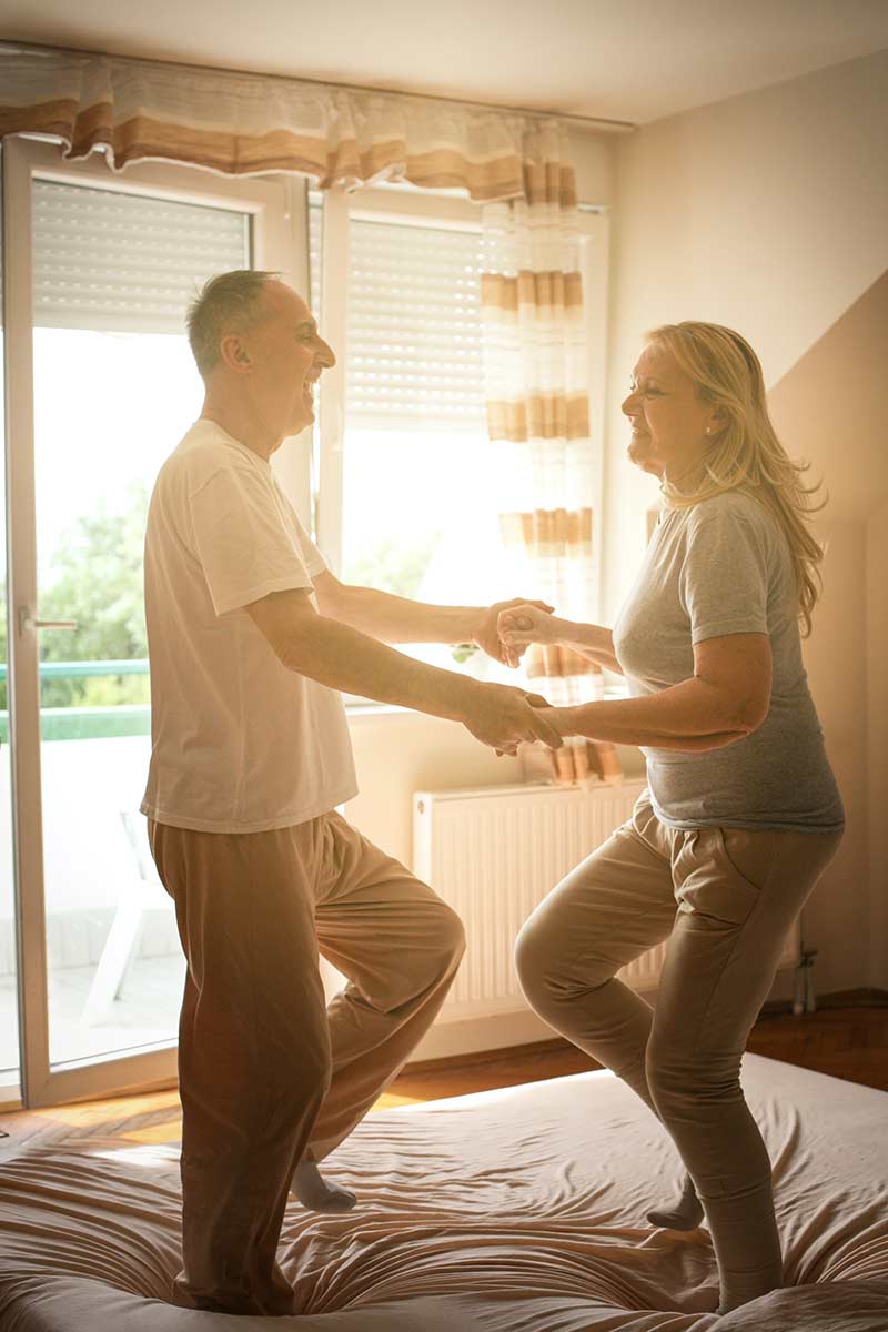 A man and woman joyfully dancing together on a bed, showcasing a moment of happiness and connection because of their successful couple conseling