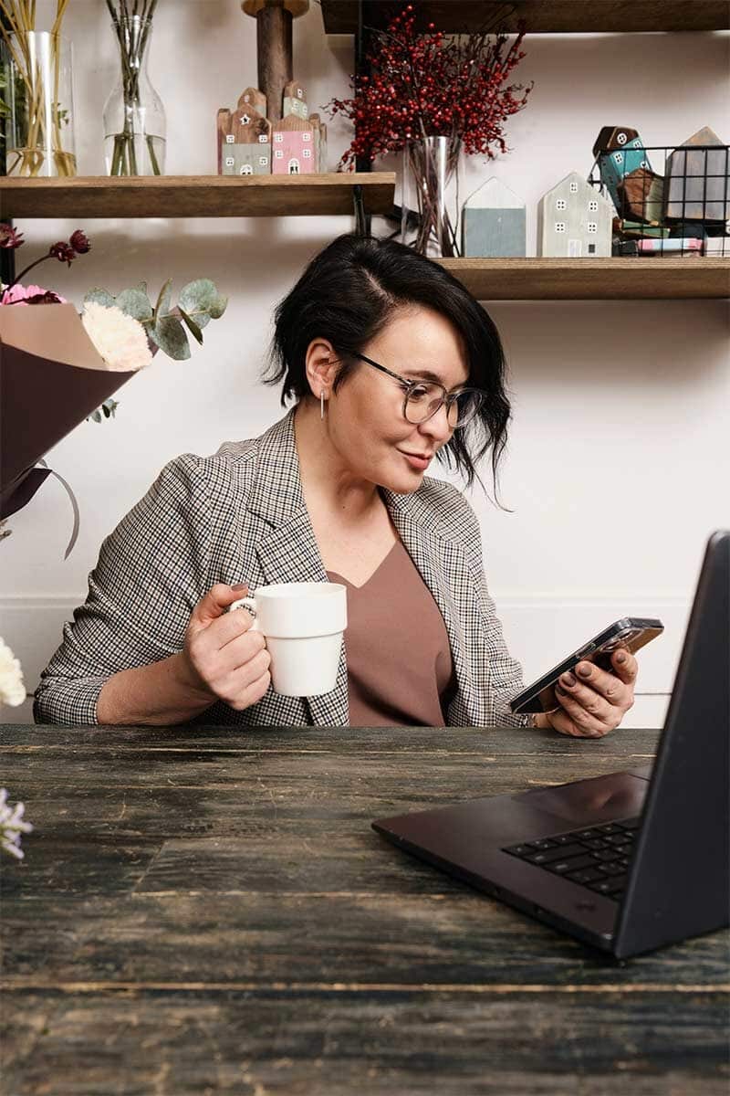 A woman using her laptop while holding a mobile phone, driven on her work because of cbt therapy. 