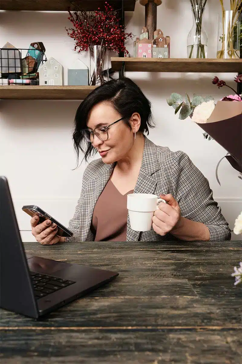 A woman using her laptop while holding a mobile phone, driven on her work because of cbt therapy. 