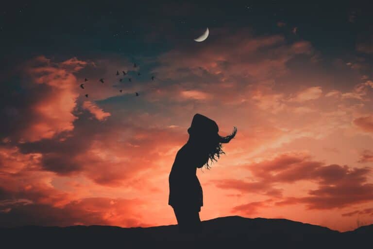 Silhouette of a person standing beneath a crescent moon during a colorful sunset, symbolizing reflection and healing through trauma-focused CBT.