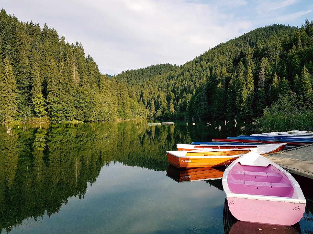 Rowboats resting on a peaceful lake surrounded by forested hills, representing calm and restoration found through trauma-focused CBT.
