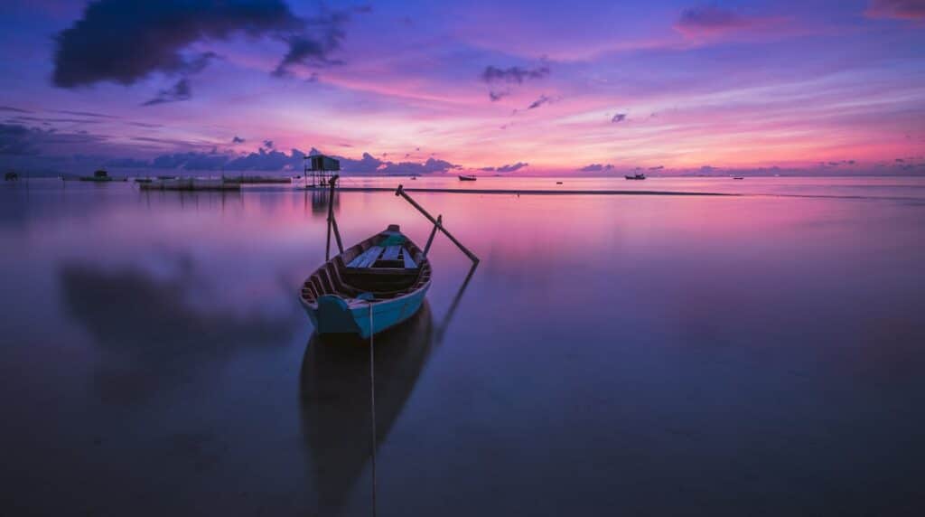 A small boat resting on calm water during a purple sunset, symbolizing peace, reflection, and emotional balance in CBT.