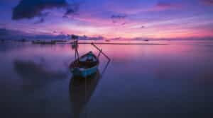 A small boat resting on calm water during a purple sunset, symbolizing peace, reflection, and emotional balance in CBT.