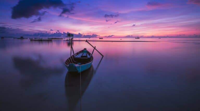 A small boat resting on calm water during a purple sunset, symbolizing peace, reflection, and emotional balance in CBT.