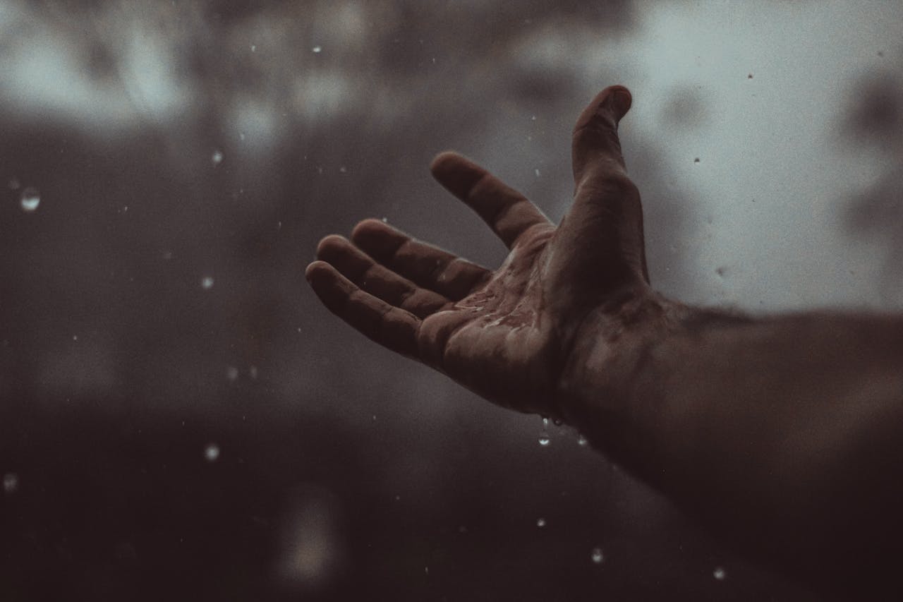 Outstretched hand in the rain symbolizing emotional overwhelm and uncertainty linked to complex trauma.