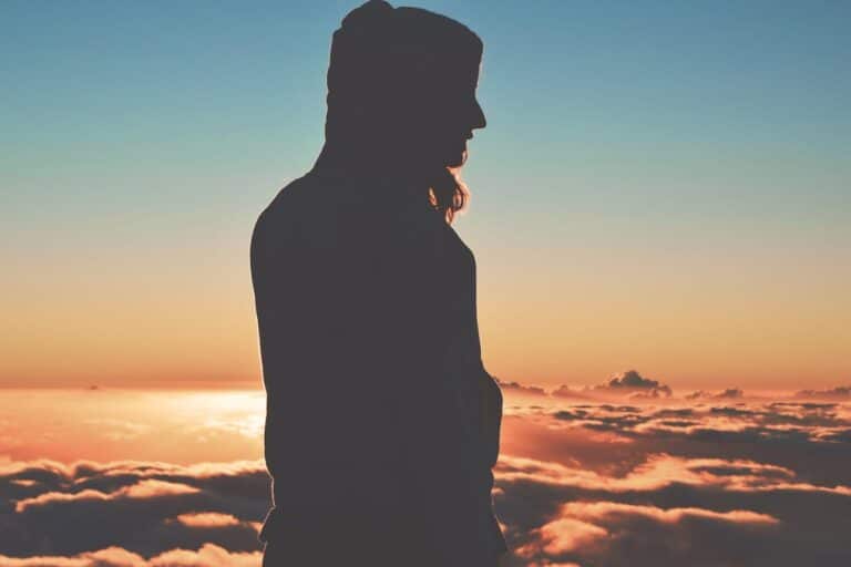 Silhouette of a person standing above the clouds at sunset, symbolizing emotional overwhelm and reflection.