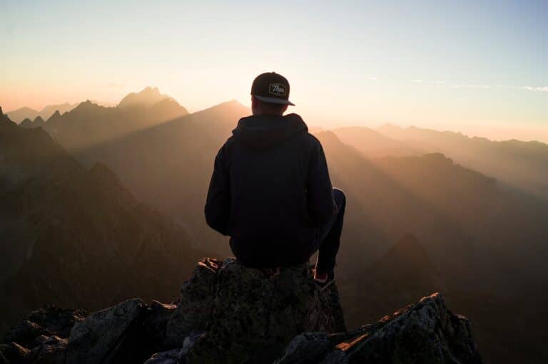 Person sitting on a mountain at sunrise representing reflection, tension, and difficulty relaxing due to hypervigilance.