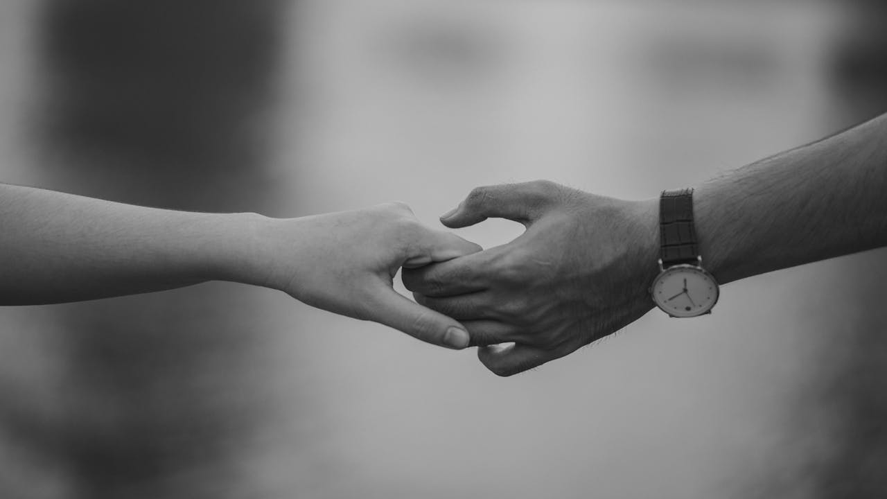 Black and white image of two people holding hands, representing trust, vulnerability, and attachment wounds in adult relationships