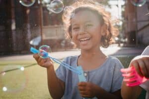 Child smiling and playing with bubbles representing healing and emotional recovery from childhood trauma through CBT