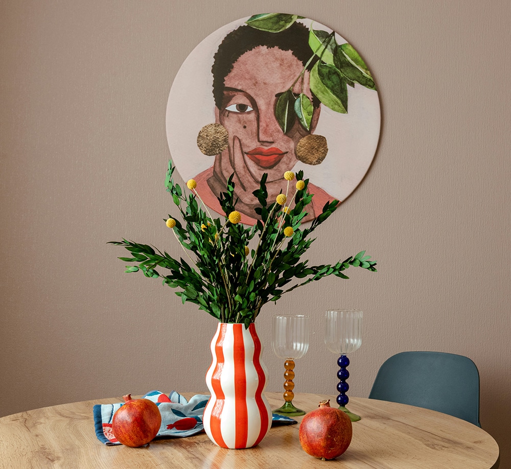A stylish wooden table set with two pomegranates, a red-and-white striped vase of yellow flowers