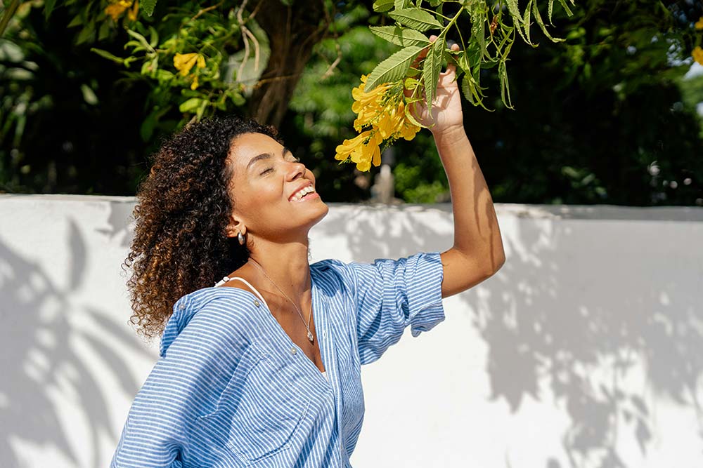 a woman in a blue shirt is picking flowers from a tree