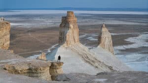 A person standing on a rocky desert cliff overlooking a vast, rugged landscape.