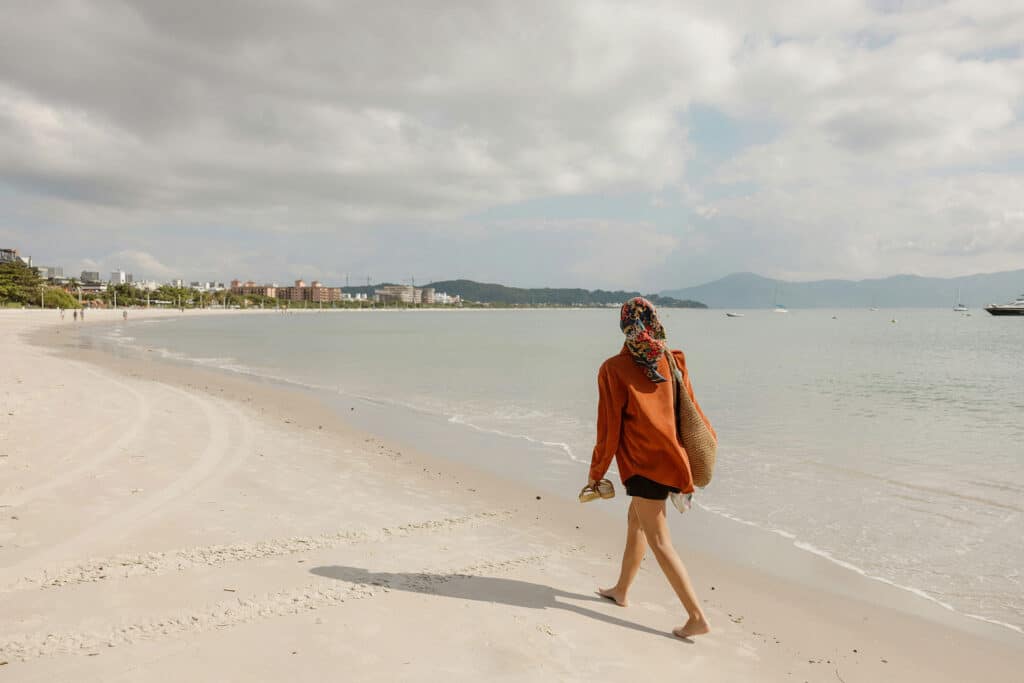 Woman walking barefoot on a calm beach with distant buildings